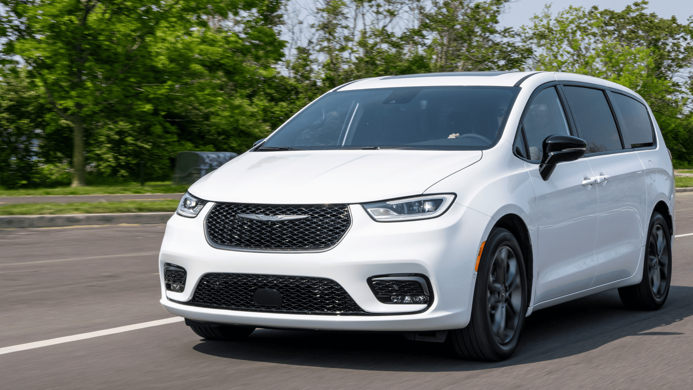 Front angle of 2026 Chrysler Pacifica in motion on the road, showcasing black grille and sleek headlights.