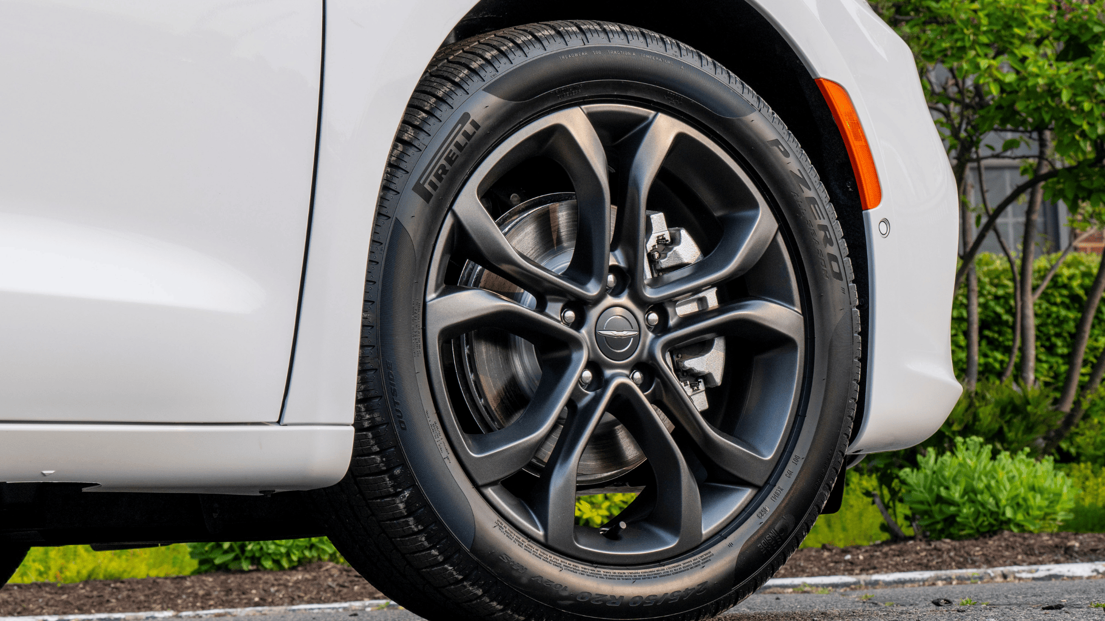 Close-up of 2026 Chrysler Pacifica Pirelli tire and black alloy wheel design on white exterior.