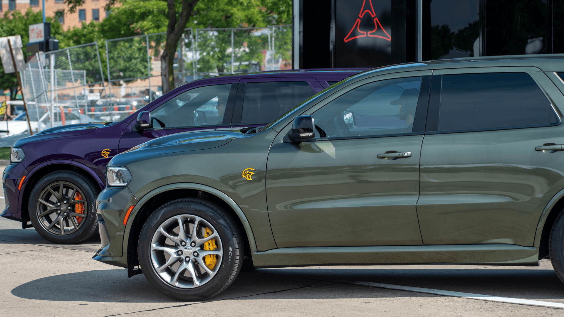 Side profile of green and purple 2026 Dodge Durango SUVs in outdoor display, showing Hellcat badge and Brembo brakes.