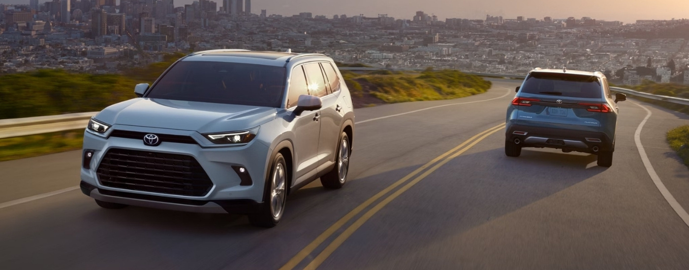 A white and a blue 2025 Toyota Grand Highlander going opposite directions.