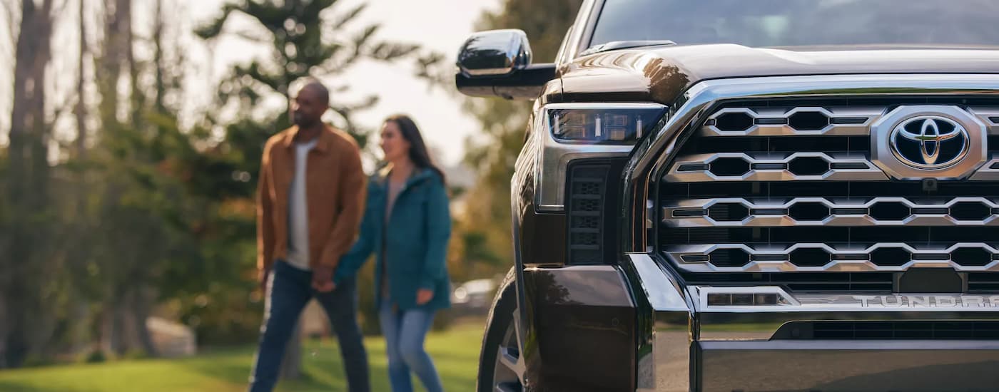 Couple walking behind a black 2023 Toyota Tundra used truck for sale at a dealer