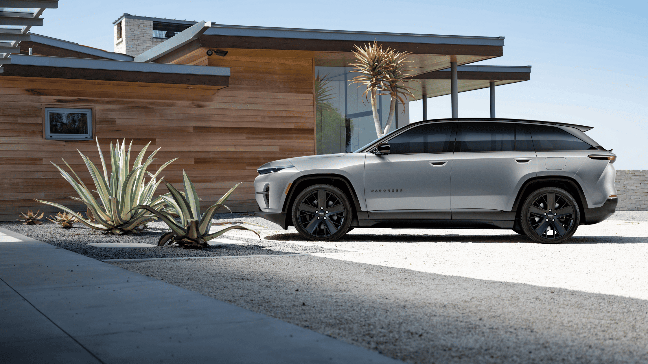 2025 Jeep Wagoneer S exterior side view in silver with modern home backdrop.