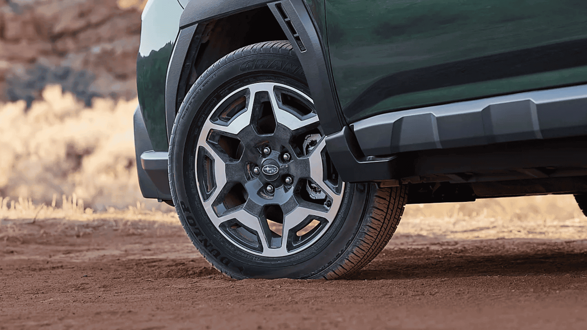 Close-up of 2026 Subaru Outback alloy wheel and tire on red dirt terrain.