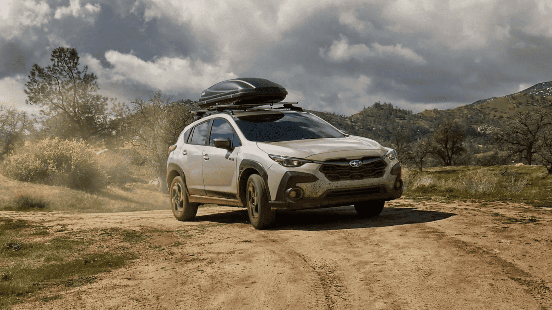 2026 Subaru Crosstrek Hybrid driving on a dirt trail with a roof cargo box in Beckley WV.
