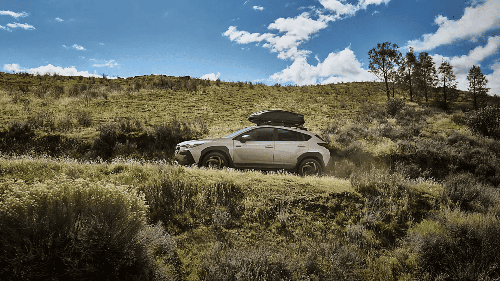 Side profile of 2026 Subaru Crosstrek Hybrid crossing grassy hills under a blue sky.