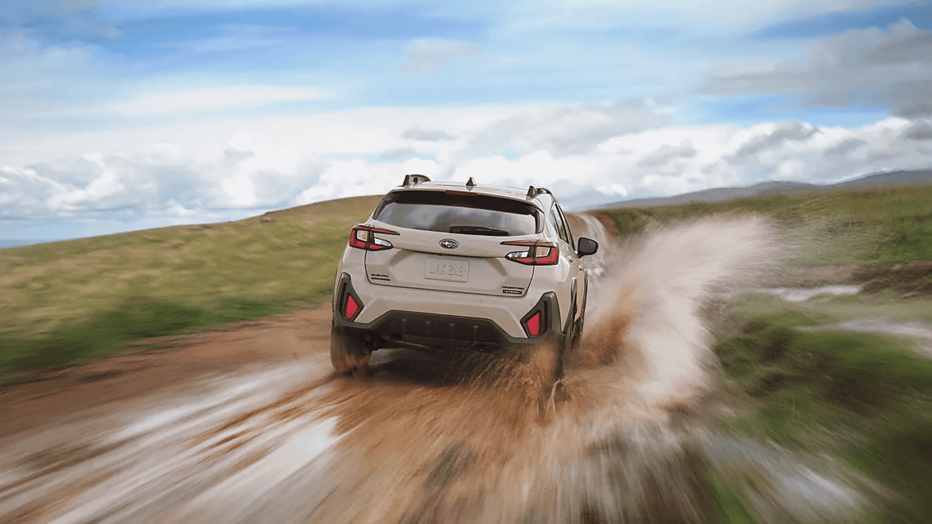 Rear view of 2026 Subaru Crosstrek Hybrid kicking up water while driving through a muddy path.
