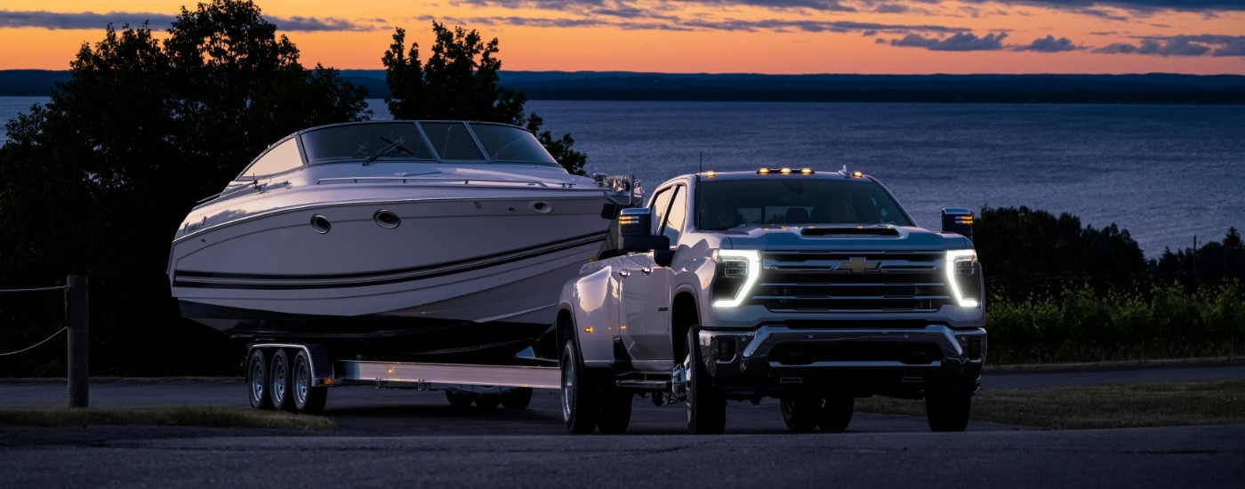 A white 2025 Chevy Silverado 3500 from the front while towing a boat.
