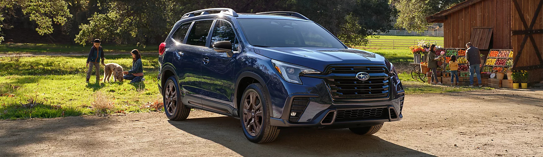 a blue 2025 subaru ascent parked next to a barn