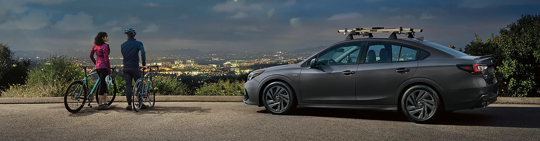 2025 subaru legacy parked at an overlook with people on bikes next to it at night