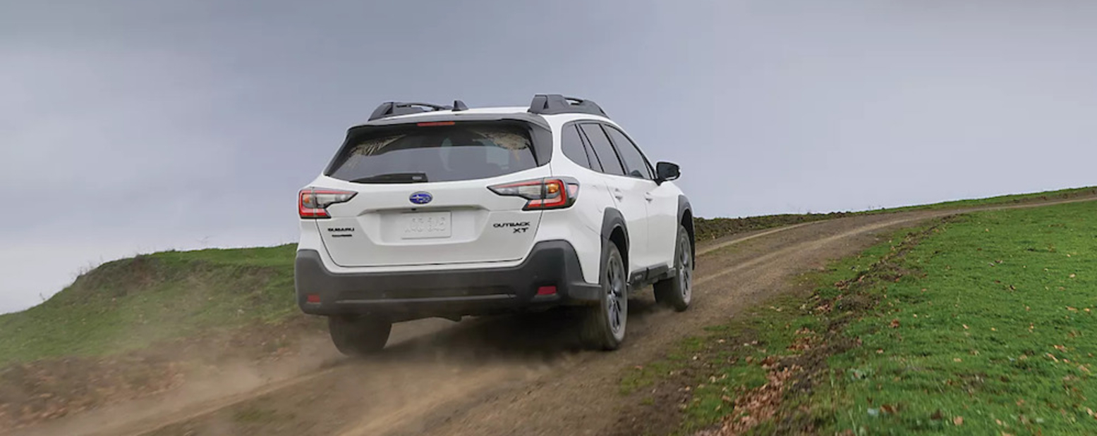 The back of a white Subaru Outback driving down a dusty road