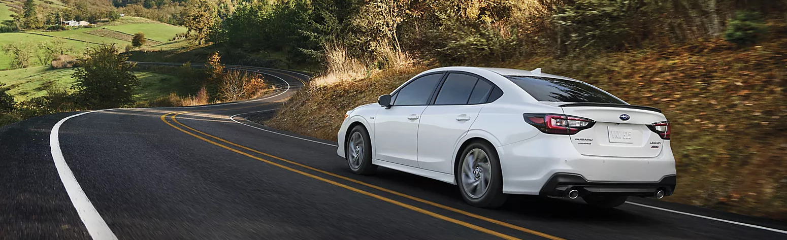 a white 2025 subaru legacy driving on a winding road