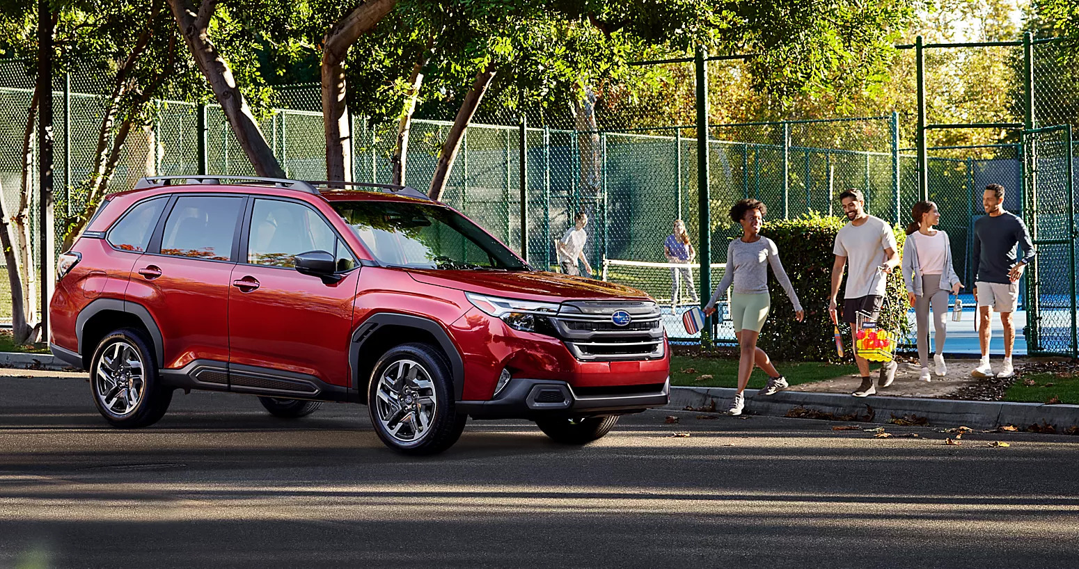 a red 2025 subaru forester parked next to a park with people around