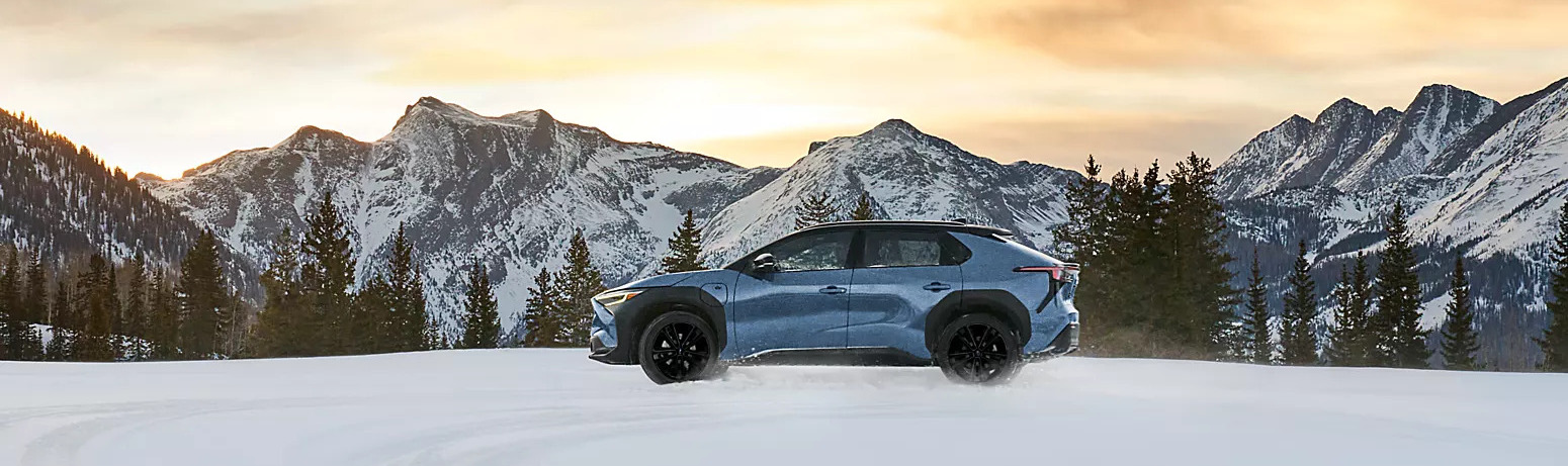 a blue 2025 subaru solterra parked in the mountains with snow covering the ground
