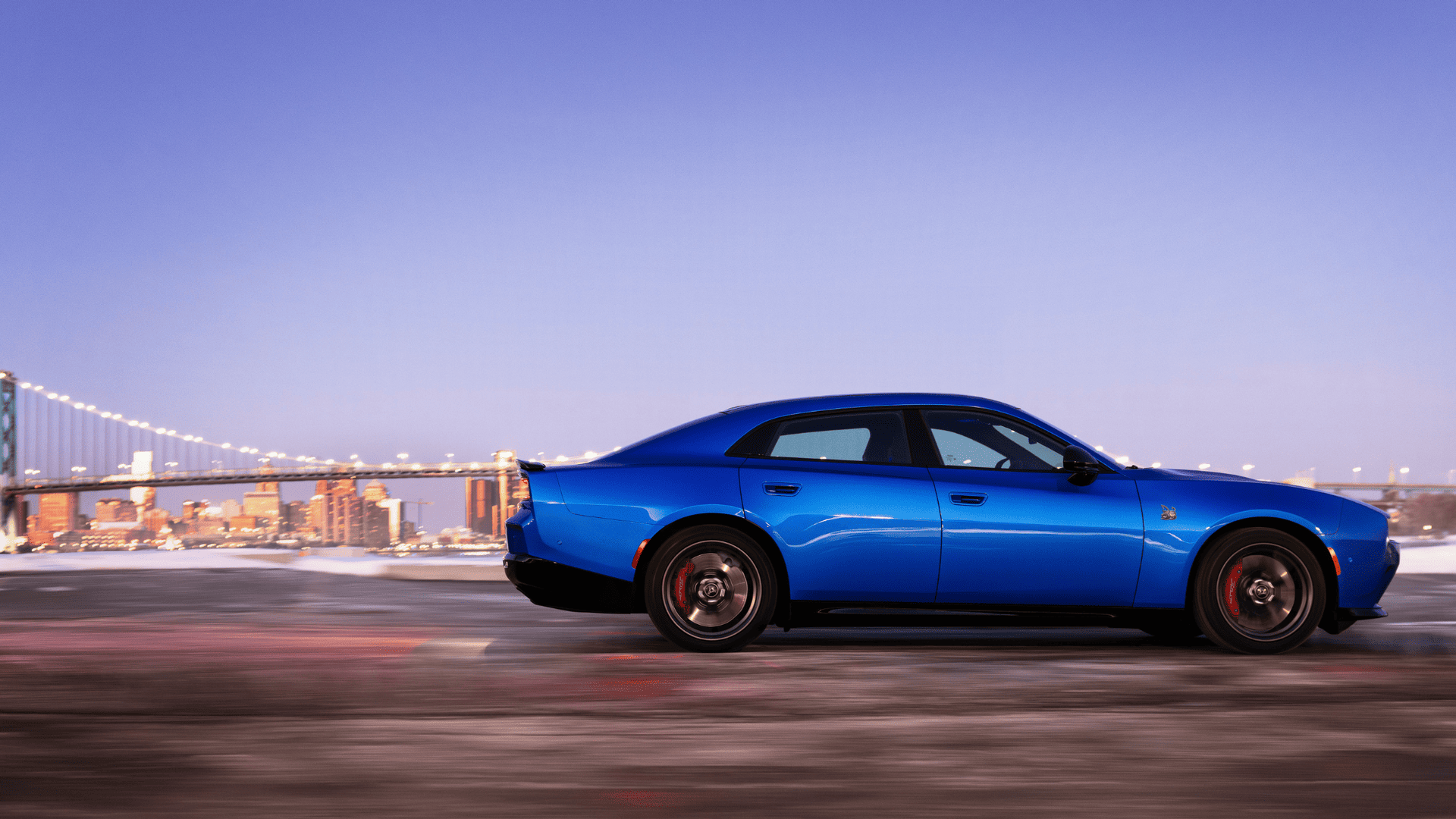 2026 Dodge Charger Daytona in blue speeding past city skyline with bridge in the distance.