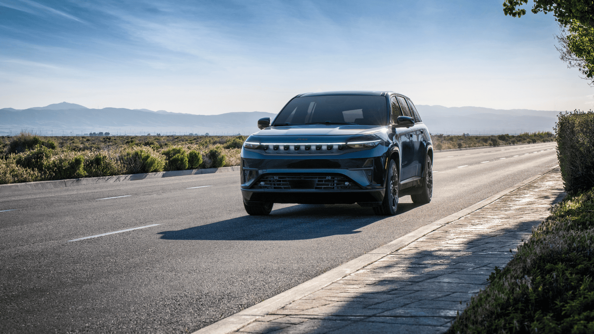 2025 Jeep Wagoneer S electric SUV driving on open road with mountain views in the background.