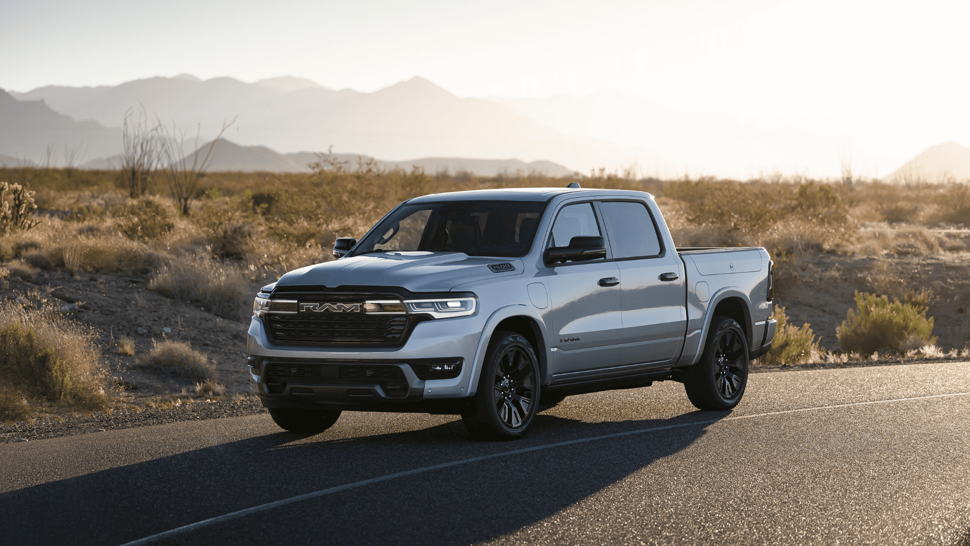 2026 Ram 1500 pickup truck parked on desert road with rugged mountain scenery in the distance.