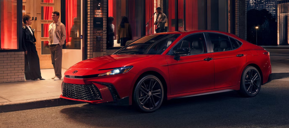 A side view of a red 2026 Toyota Camry parked on nighttime city street
