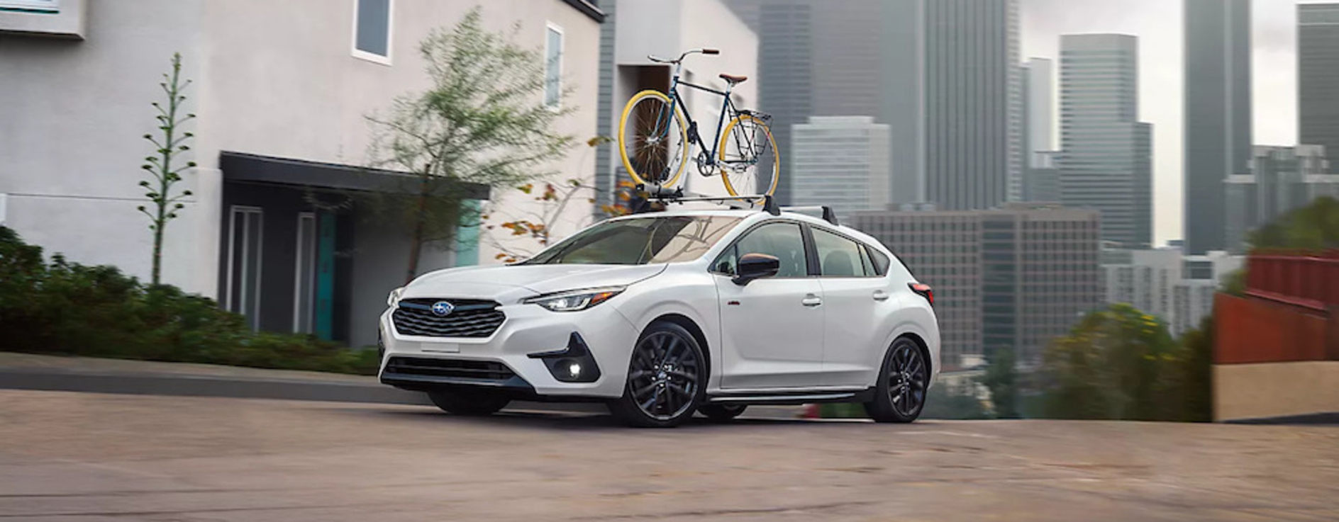 A white 2026 Subaru Impreza with a bicycle on its roof driving down a city street
