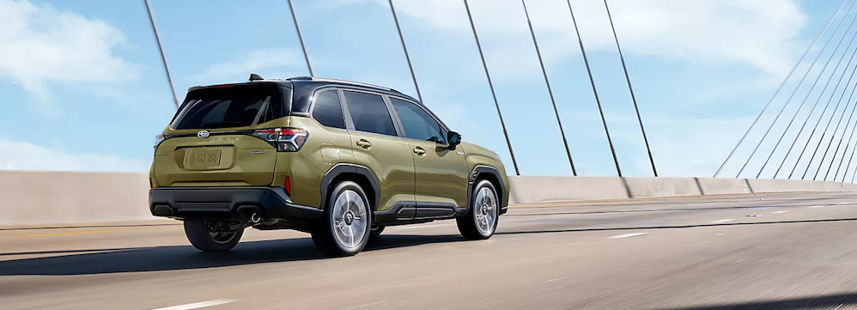 A green 2025 Subaru Forester Hybrid SUV driving across a bridge