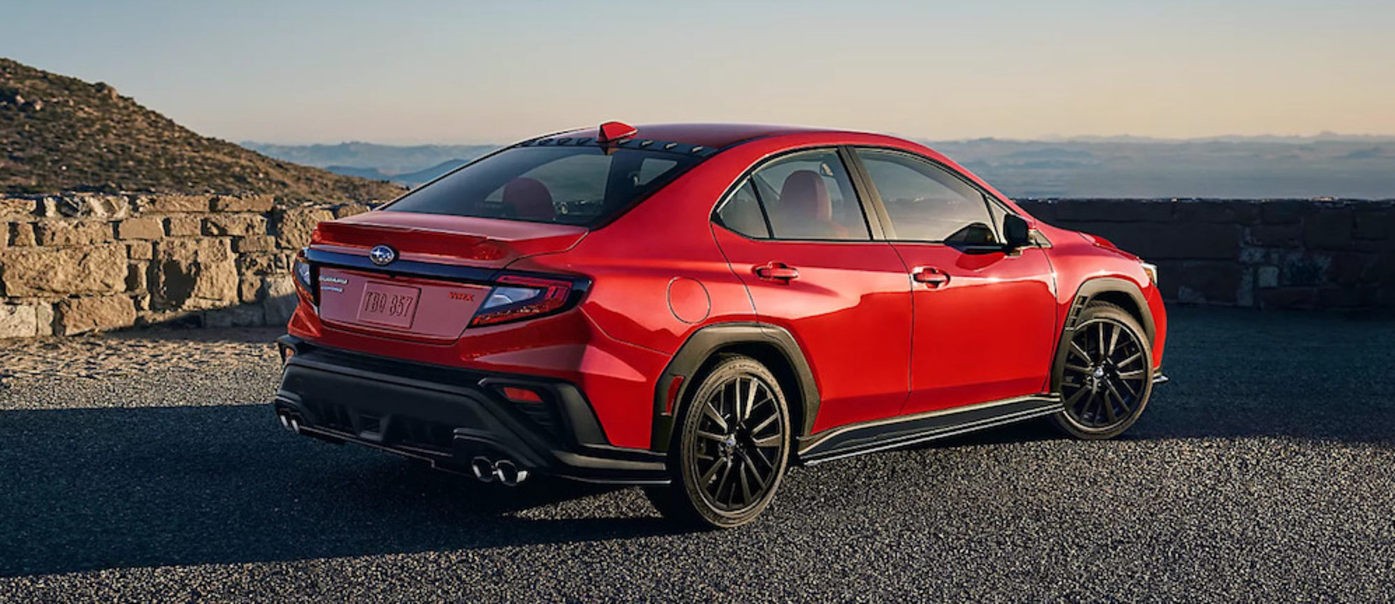 A red 2025 Subaru WRX sports car parked on a mountainside at sunset