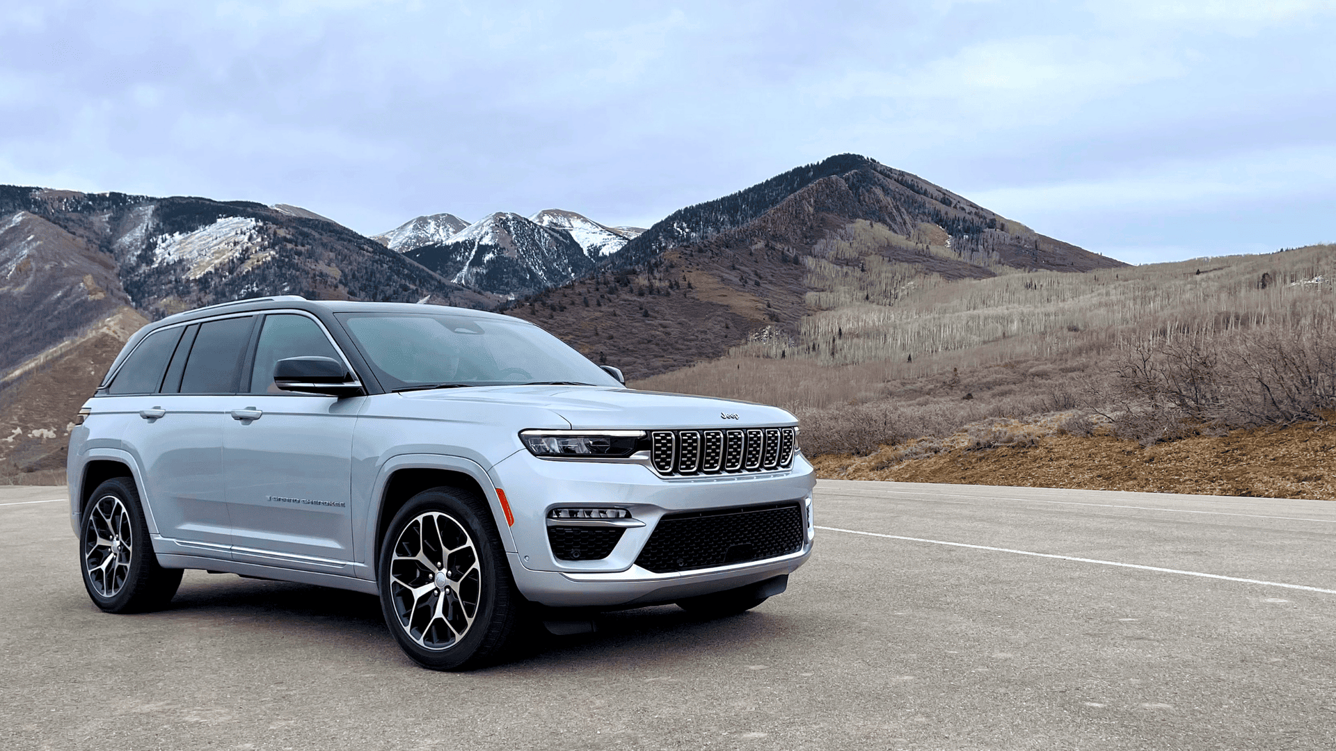 Exterior view of a silver 2026 Jeep&reg; Grand Cherokee parked in front of snow-capped mountains.