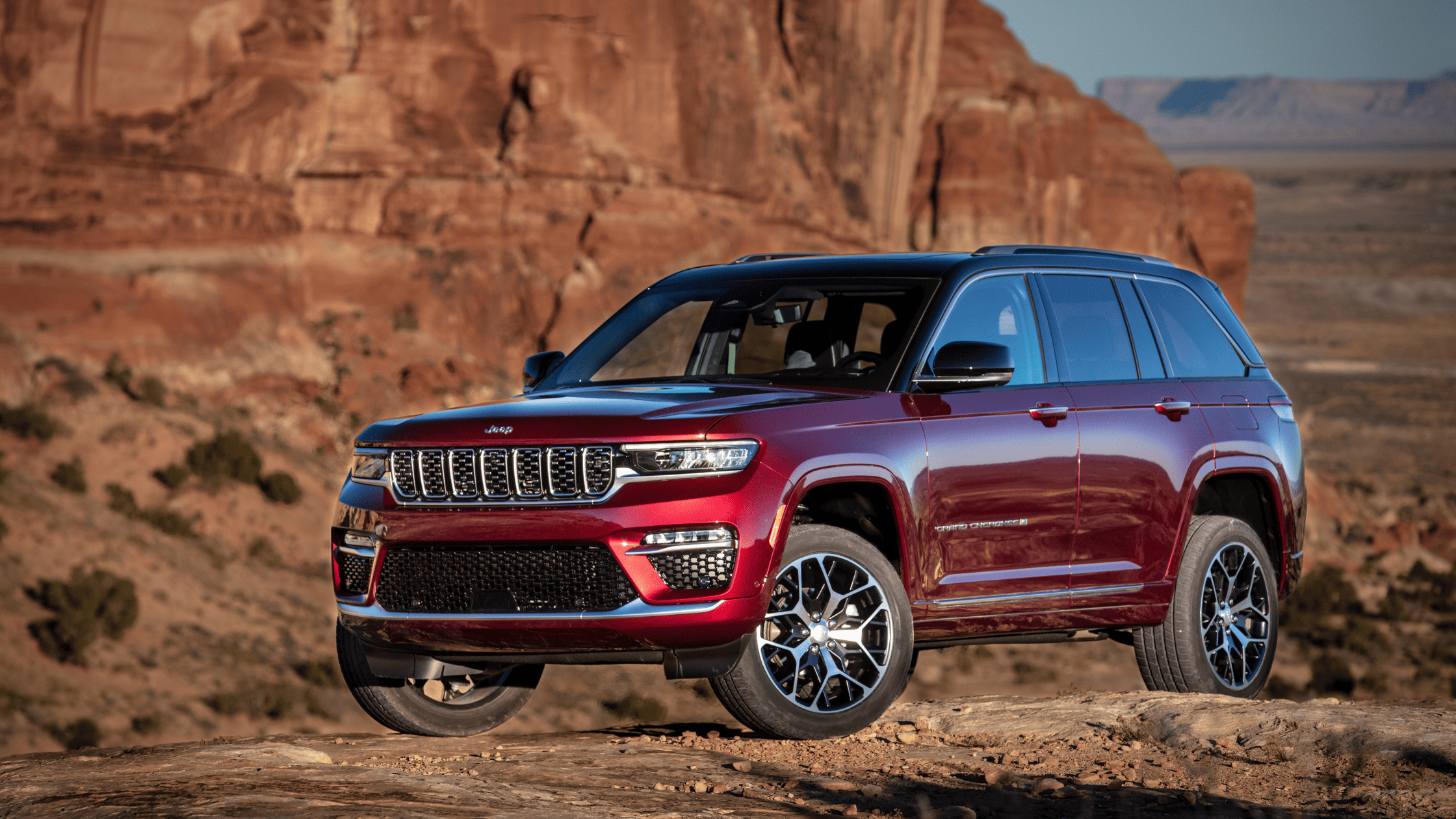 2026 Jeep&reg; Grand Cherokee in red metallic finish parked near canyon cliffs highlighting rugged design.