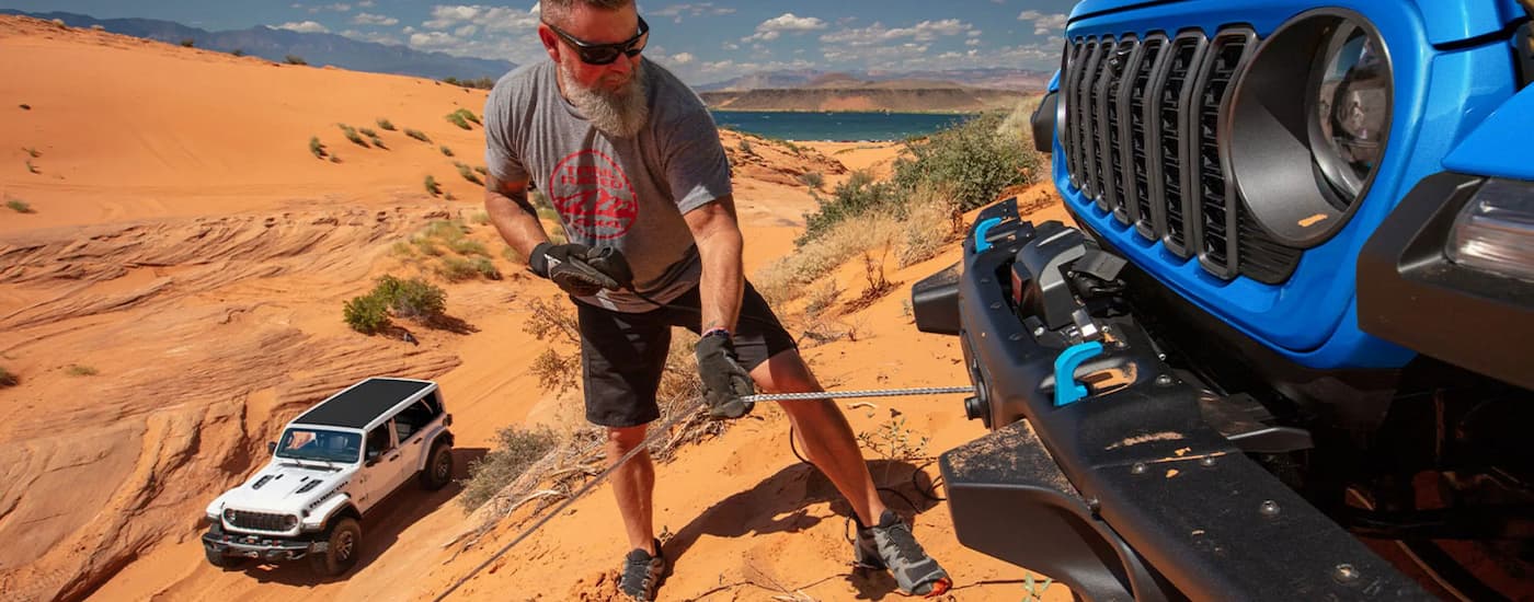 Man using the winch on the front of a blue 2025 Jeep Wrangler for sale