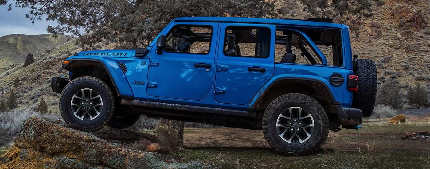 Side of a blue 2025 Jeep Wrangler Rubicon off-roading on a rocky trail