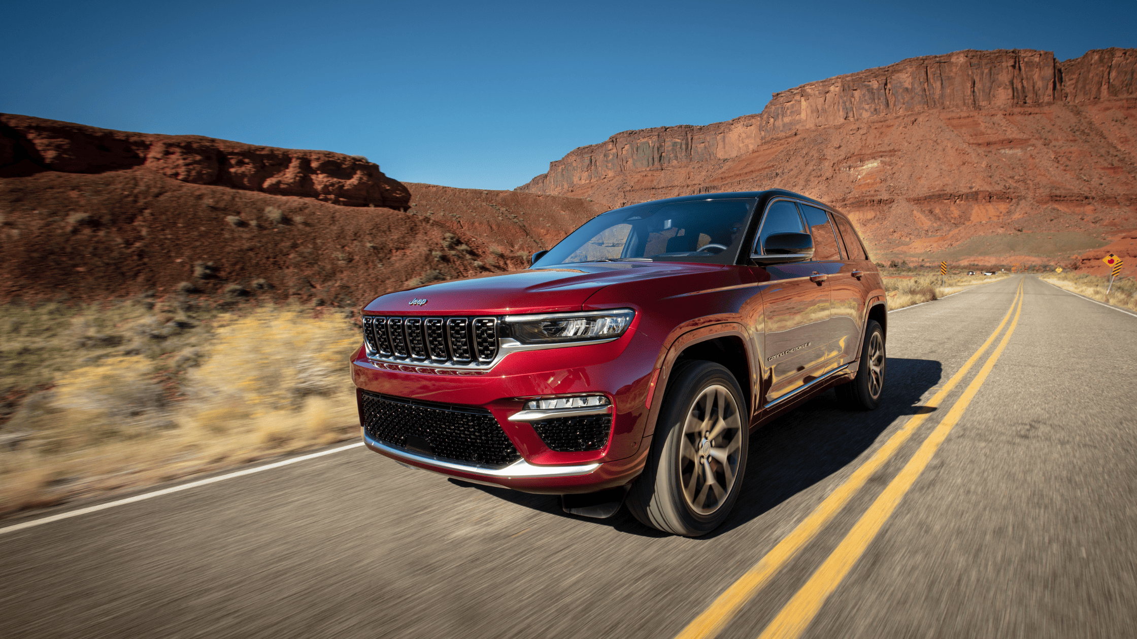 Front angle view of the 2026 Jeep&reg; Grand Cherokee driving through desert terrain under clear skies.