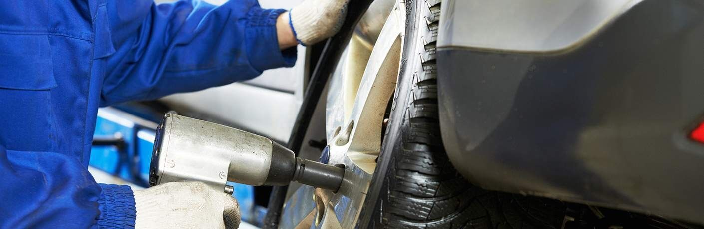 A gloved mechanic uses a drill to loosen a bolt in a hubcap.