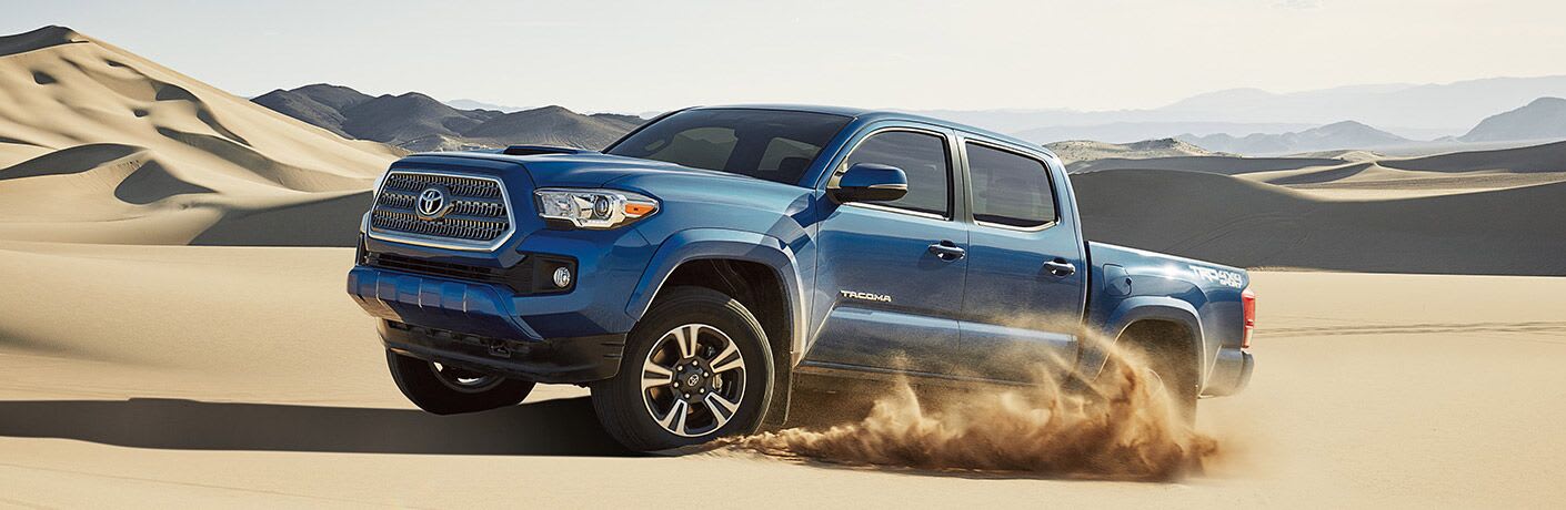 2017 Toyota Tacoma emerges from under the sand in the midst of a vast desert.