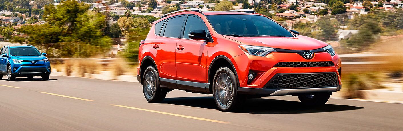 Orange 2017 Toyota RAV4 drives up a highway, with a blue model behind it.