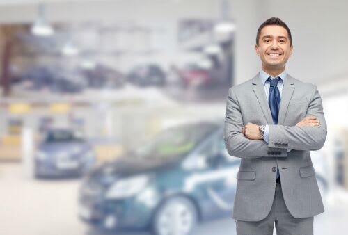 A well-dressed salesman crosses his arms and smiles in a showroom.
