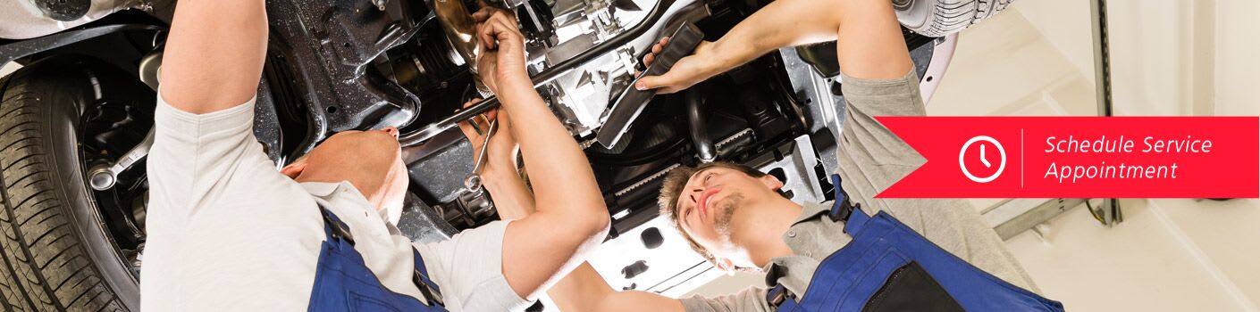 Two men work on the underside of a car