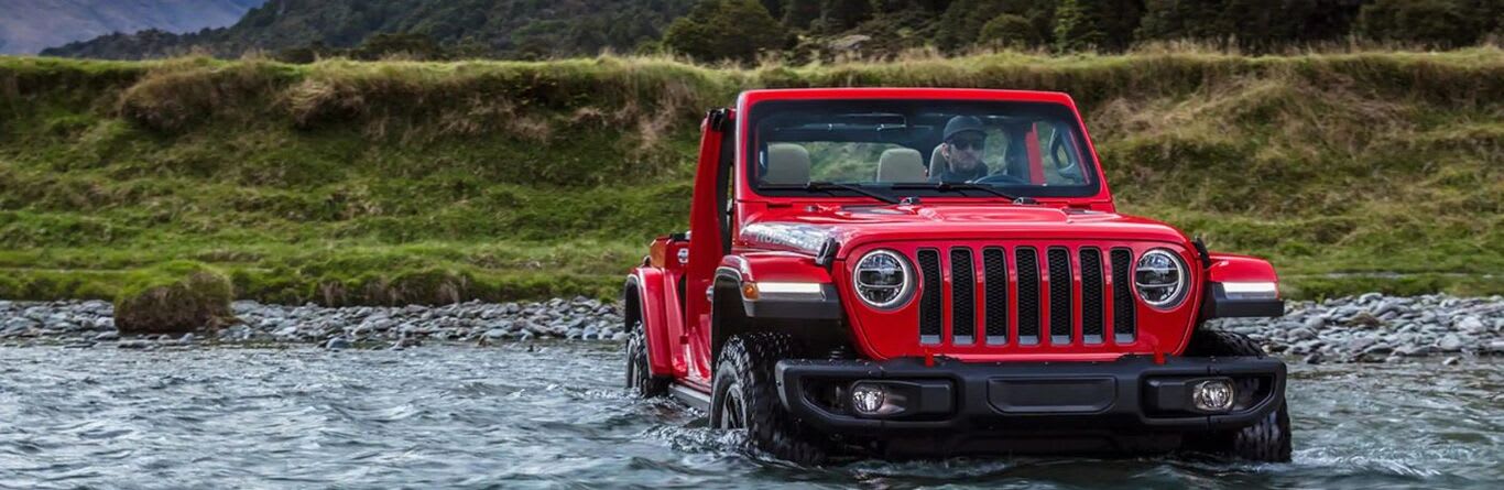 A person driving the 2023 Jeep Wrangler through a river stream.