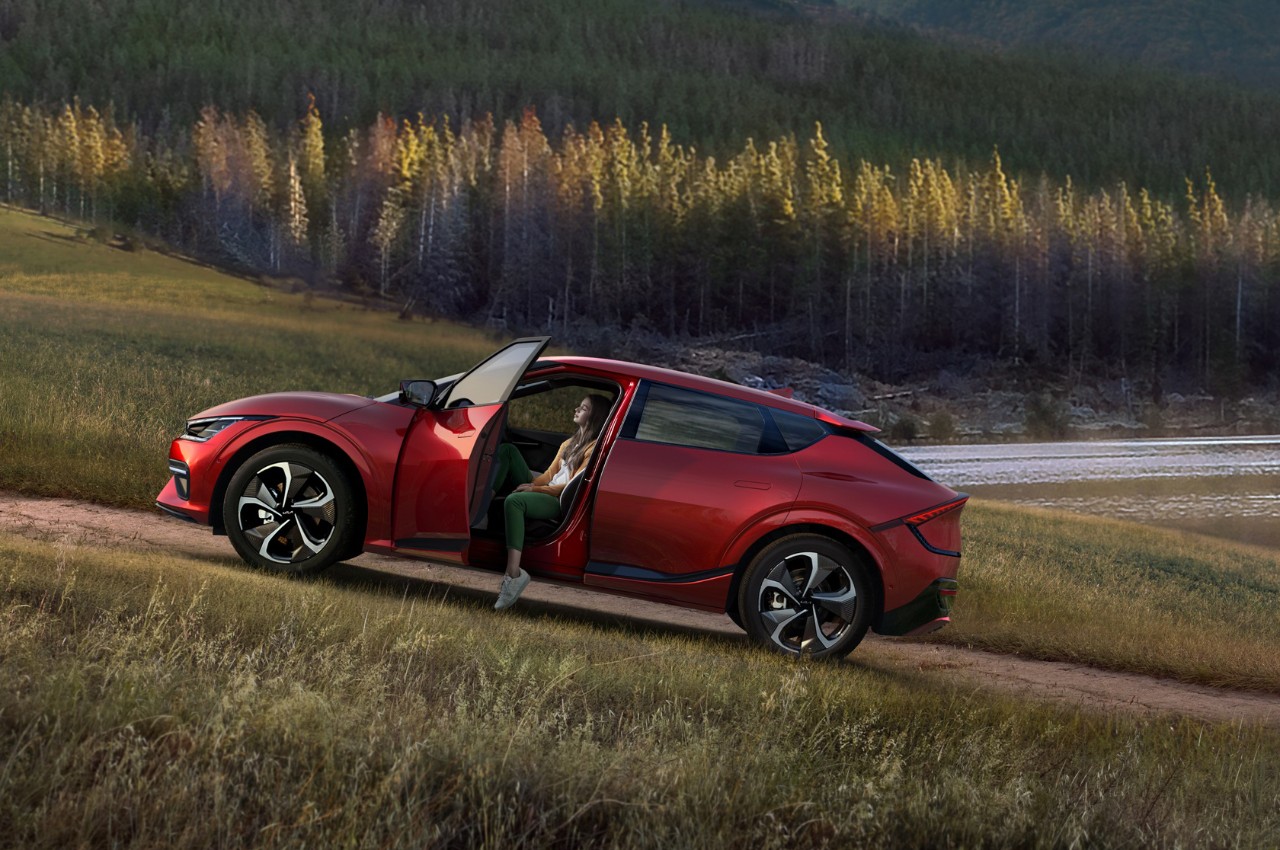 Red Kia parked on a hill, with the door open and the drivers leg hanging out