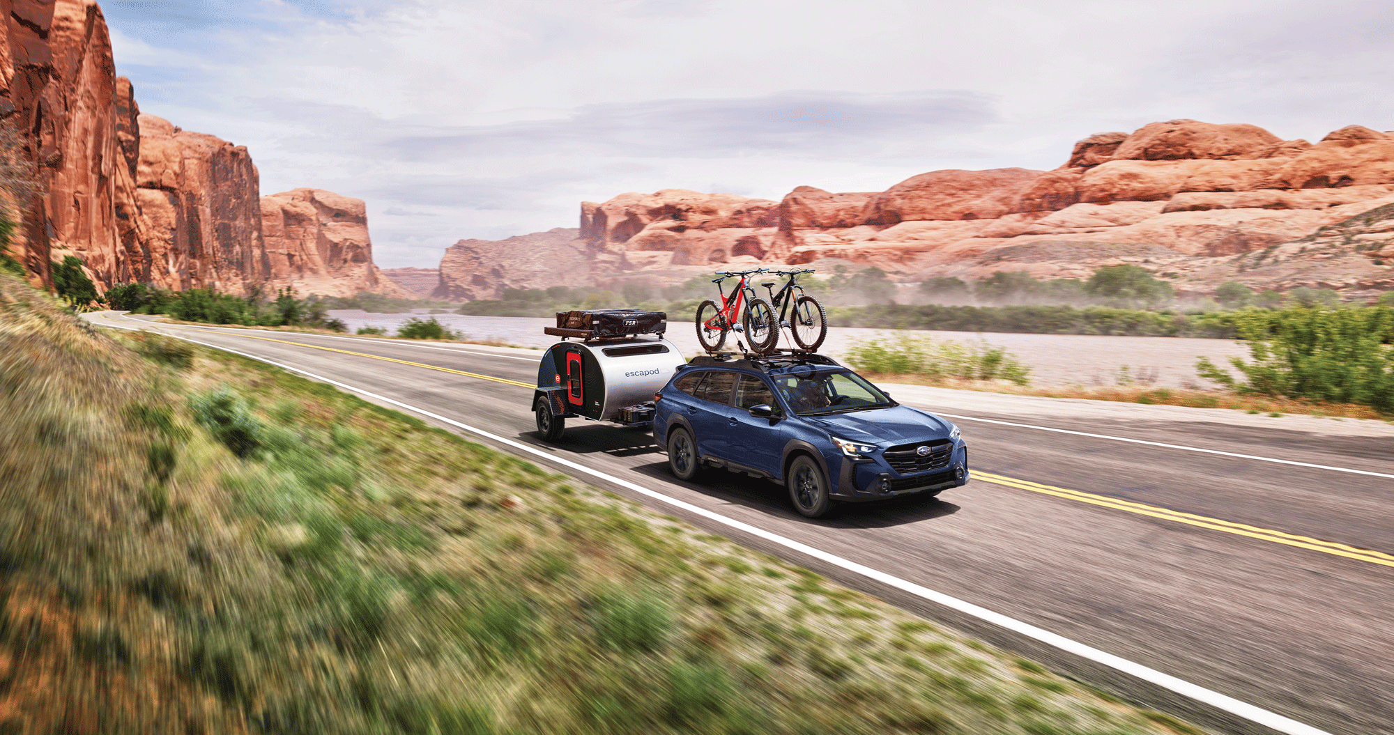 A 2023 Outback towing a camper trailer on a desert highway.
