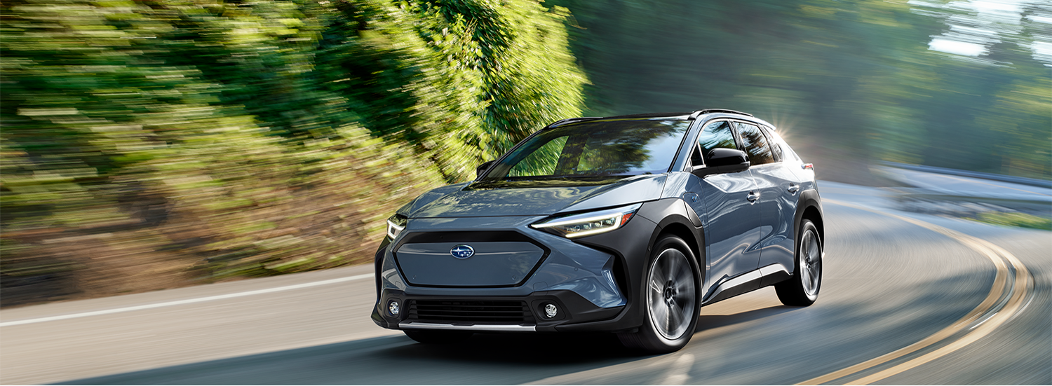 A 2025 Subaru Solterra AWD EV rounds a corner on a country highway.