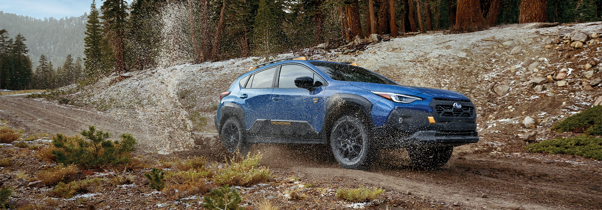 A Crosstrek Wilderness all-wheel drive SUV splashes through a puddle on a dirt road.
