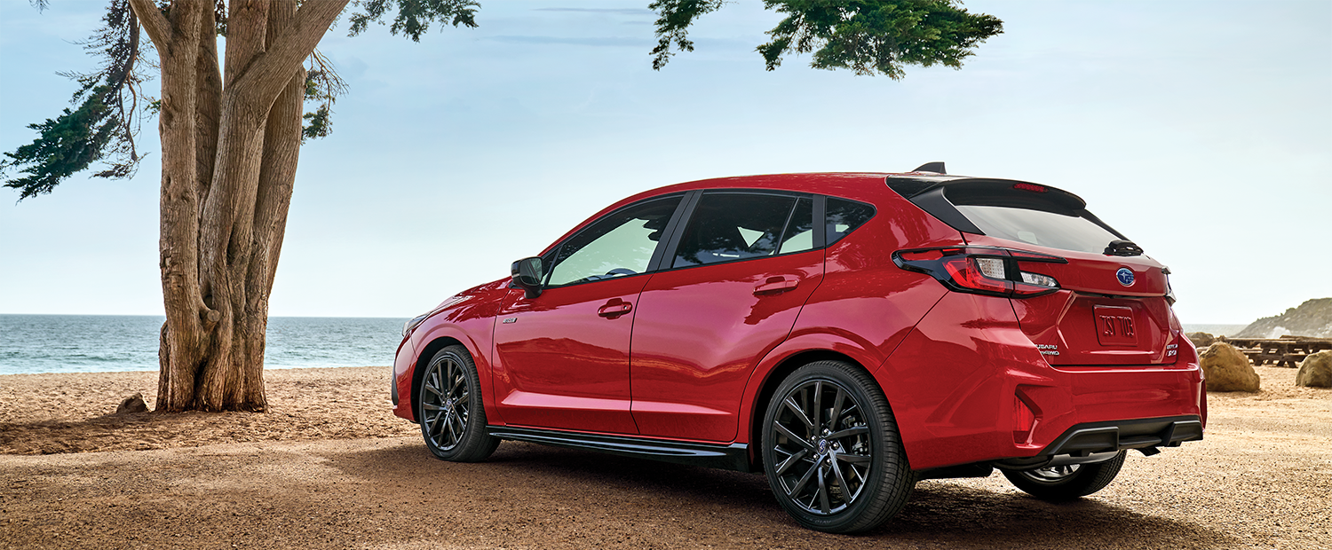 A red Impreza AWD hatchback parked by the ocean.