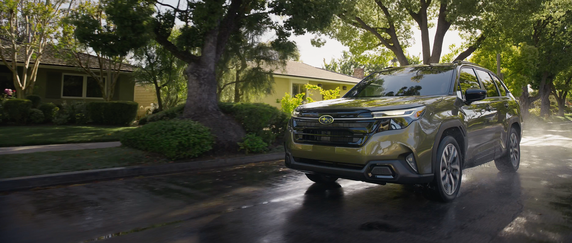 2025 Subaru Forester Hybrid driving on a wet, tree-lined neighborhood street.