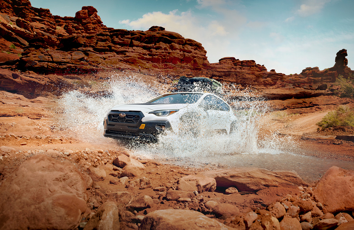 A white 2024 Subaru Crosstrek AWD subcompact SUV splashes through a puddle on a canyon trail.