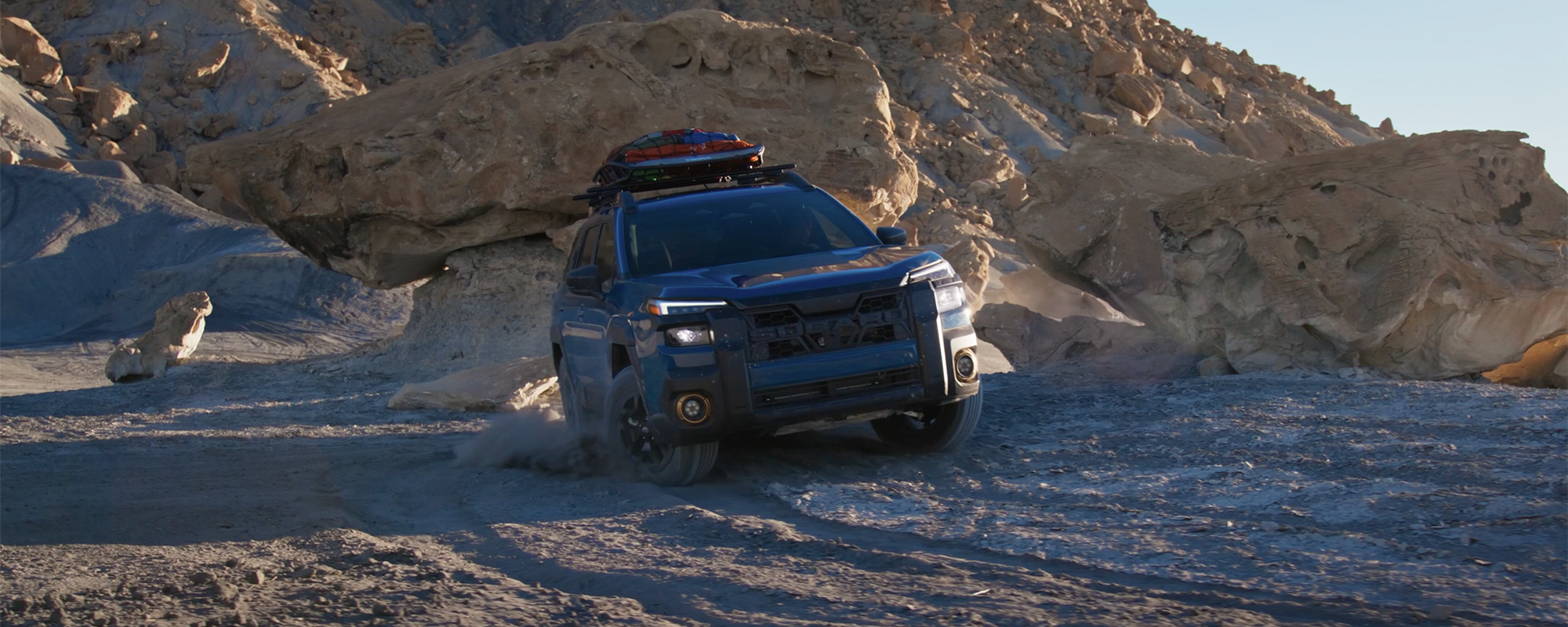 A geyser blue 2026 Subaru Outback Wilderness AWD SUV driving through various features of a desert biome.