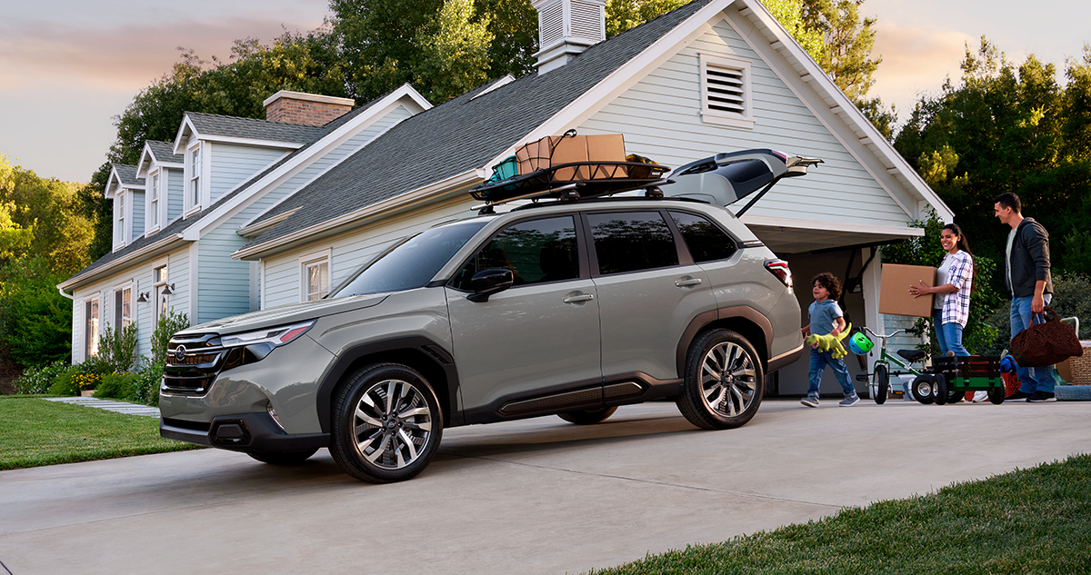 A family stands by a Subaru Forester with boxes and camping gear on its roof rack.