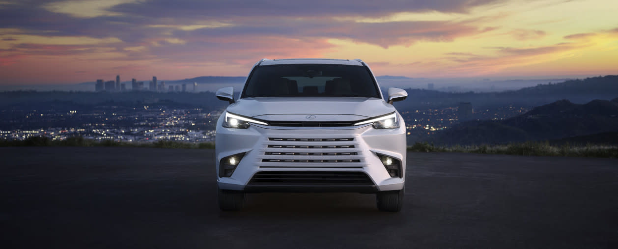 Image of a white 2025 Lexus TX on a hill overlooking a city at sunset