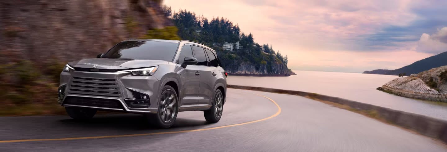 Image of a grey 2025 Lexus TX driving along a curvy lakeside road