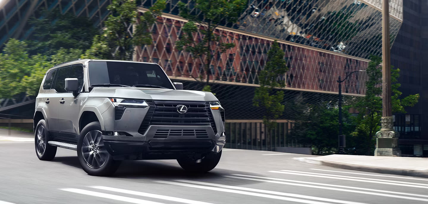 Image of a silver 2025 Lexus GX 550 driving on a city street