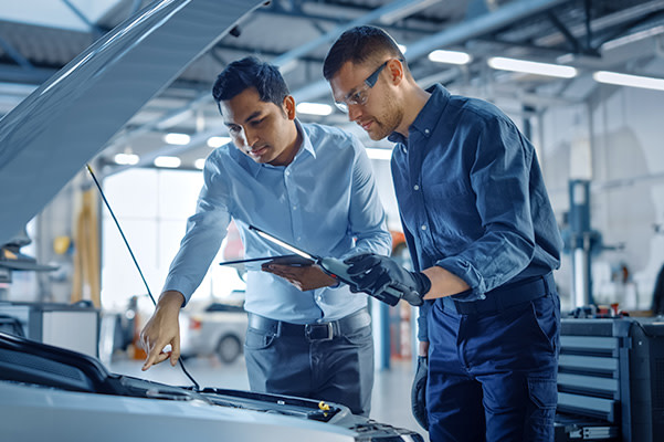 Shot of technician in training with supervisor looking under hood of car.