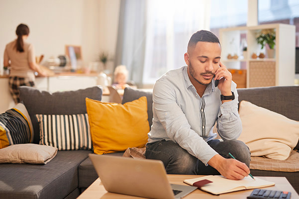 Person sitting on couch on the phone writing stuff in notepad.